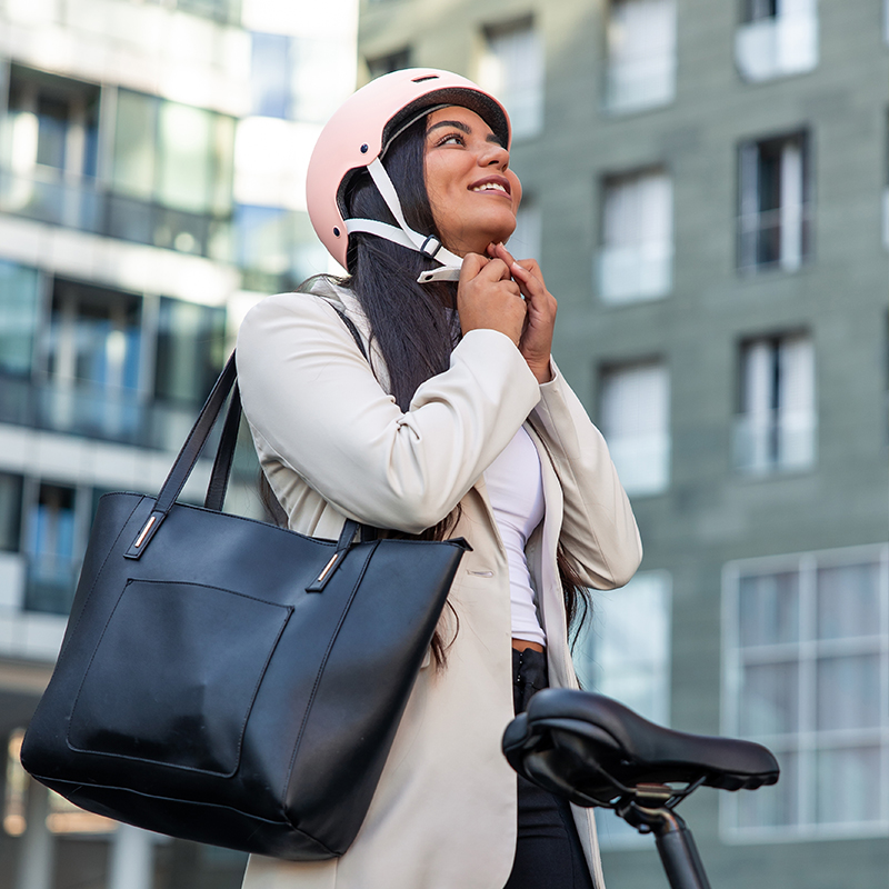 MezzoOnWalnut_BikeCommuter_Square-Web Bike Commuter woman putting on helmet with work bag